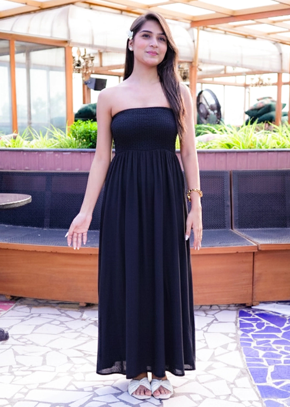 Woman in a black strapless dress standing outdoors with plants and furniture in the background