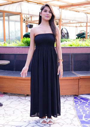 Woman in a black strapless dress standing outdoors with plants and furniture in the background