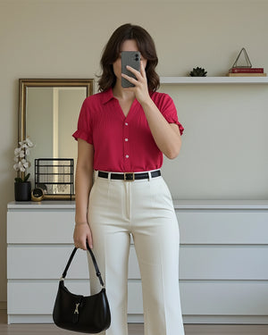 Person wearing a red shirt and white pants, holding a black handbag indoors.