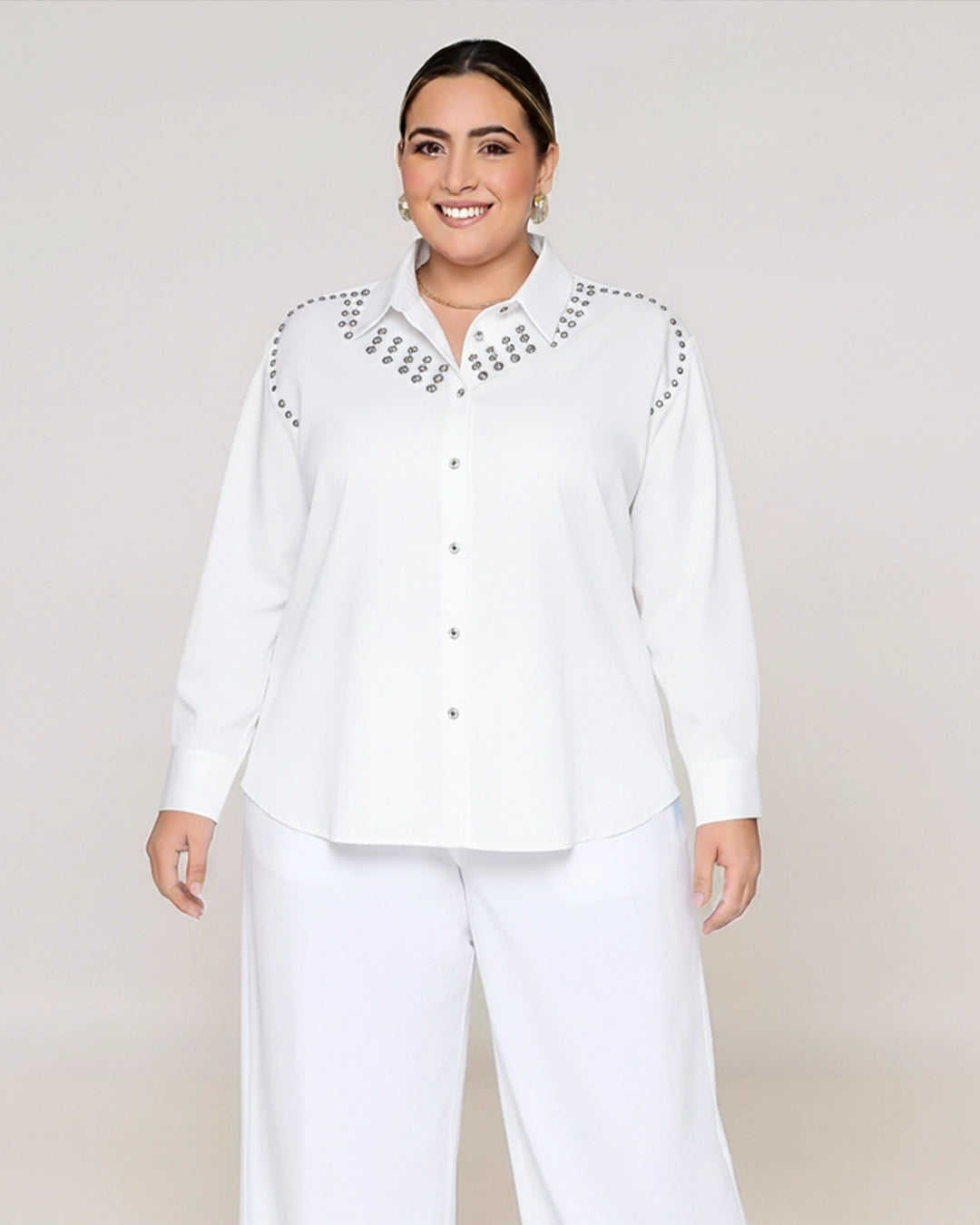 Woman wearing a white blouse with embellishments on a plain background