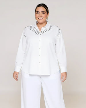 Woman wearing a white blouse with embellishments on a plain background