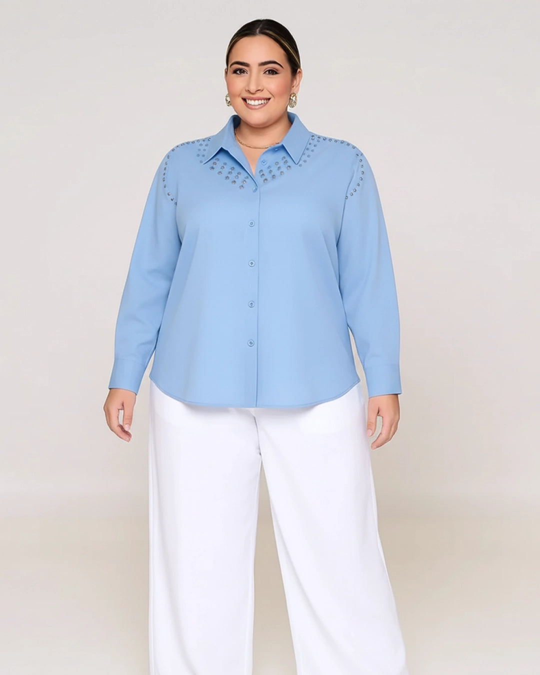Woman wearing a light blue button-up shirt with decorative studs and white pants on a plain background
