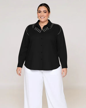 Woman wearing a black shirt with studded collar and white pants on a plain background